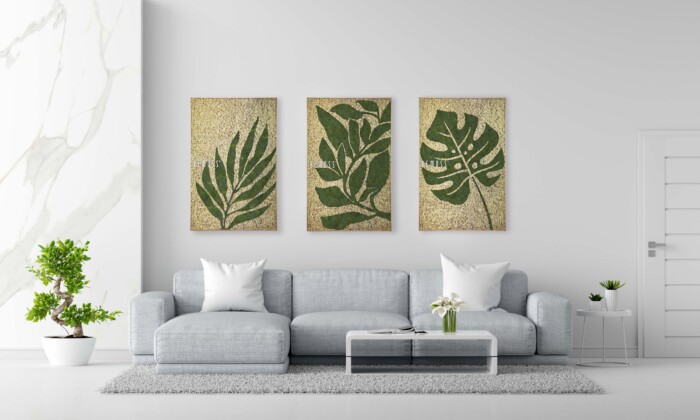 Un salon moderne avec un canapé gris clair orné de coussins blancs. Au-dessus du canapé se trouvent trois œuvres d’art botaniques encadrées représentant des feuilles vertes. Une petite table basse blanche avec un arrangement végétal se trouve devant le canapé et une plante en pot se trouve à gauche. Les murs présentent d'élégants Earth Rochoso, ajoutant une touche de nature à l'intérieur.