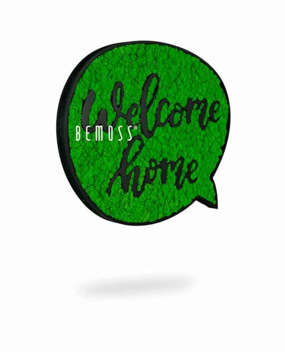 Un panneau vert circulaire avec l'expression « Bienvenue à la maison » en texte cursif noir. Le fond a un aspect texturé semblable à de la mousse, ressemblant à un Tableau de mousse Acacia (114x188cm), et le mot 