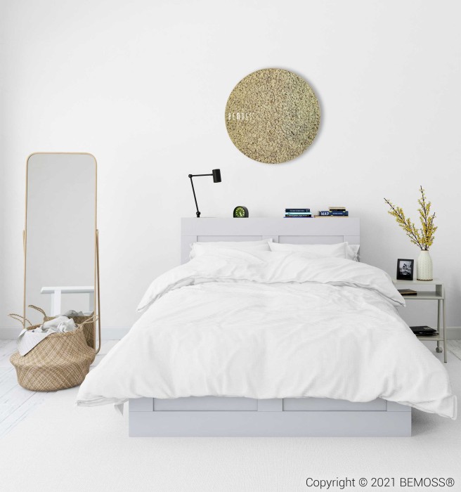 Une chambre moderne au design minimaliste comprend un lit soigneusement fait avec une literie blanche. Un miroir rond est suspendu au-dessus du lit et un grand miroir incliné se trouve à côté d'un panier tressé. Une petite table de nuit contient des fleurs jaunes dans un vase, des livres et un réveil. Le Tableau de mousse rond en mousse de RENNE mono ajoute une touche rafraîchissante à la pièce.