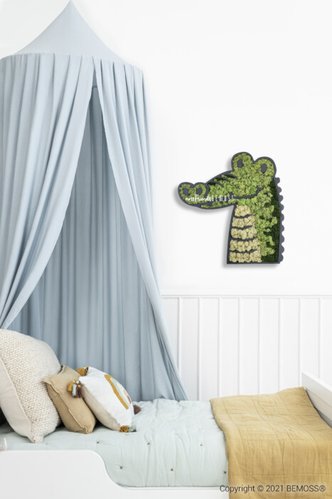 La chambre d'un enfant comprend un baldaquin au-dessus d'un berceau orné de coussins et d'une couverture jaune. Une décoration murale en forme de crocodile, réalisée à partir de feuillages verts, est accrochée aux murs clairs rehaussés de murs en mousse vibrants à côté du lit.