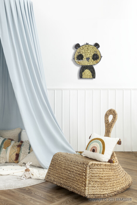 Une chambre d'enfant confortable comprend un baldaquin bleu avec des oreillers et un jouet en peluche en dessous. Un panier en osier avec une poignée et une couverture colorée se trouve à proximité. Une décoration murale en forme de panda composée de fleurs, ressemblant à un tableau de mousse, est suspendue au-dessus des lambris blancs du mur.