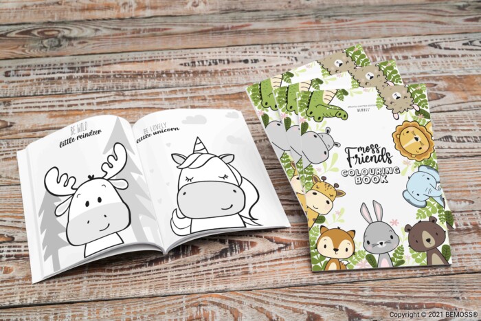 Un livre de coloriage pour enfants intitulé « My Friends Coloring Book » est ouvert sur une surface en bois. La page ouverte présente des dessins d'un élan et d'une licorne, intitulés « Petit renne » et « Petite licorne ». La couverture du livre montre divers animaux mignons, avec des fonds charmants ressemblant à des murs décorés de murs végétaux.