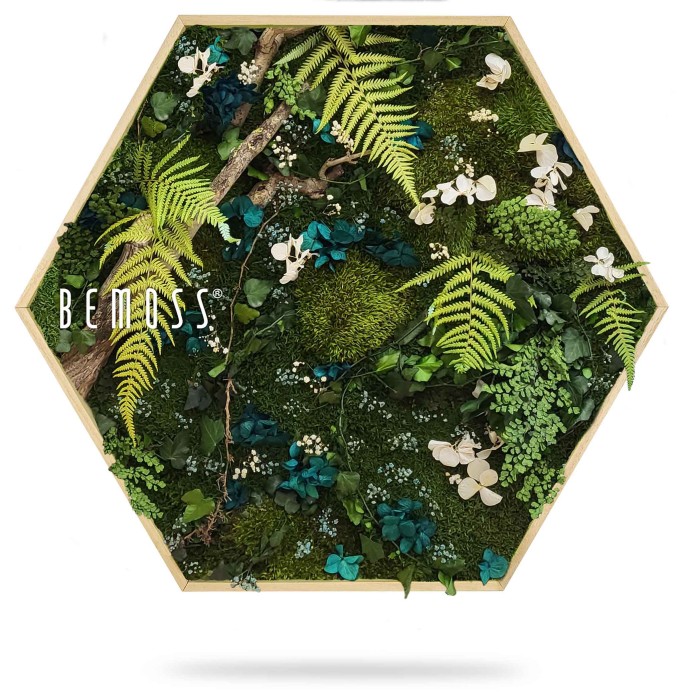 Un cadre en forme d'hexagone présente un jardin vertical luxuriant et vert comprenant un assortiment de fougères, de mousse, de petites fleurs artificielles et de feuilles. Le mot « BEMOSS » est imprimé sur le côté gauche du cadre en lettres blanches. Ce tableau de mousse unique ajoute une touche de nature à n'importe quel espace.