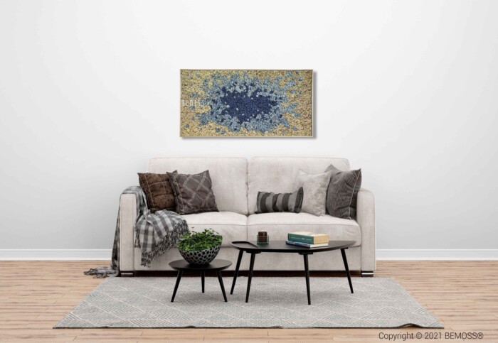 Un salon moderne avec un canapé beige orné de divers coussins et d'une couverture grise. Deux tables basses noires contiennent des livres et une plante. Un tapis gris clair repose sous les tables, tandis qu'une installation Murs végétaux ajoute une touche de nature au mur blanc présentant de grands tableaux abstraits en bleu et or.