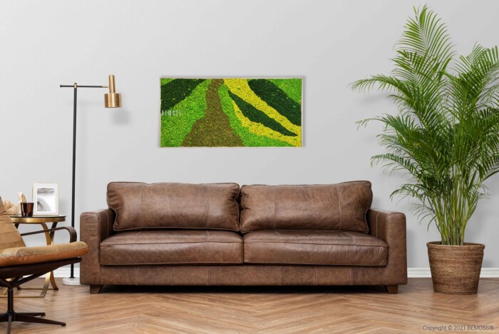 Un salon confortable comprend un canapé en cuir marron, une grande plante à feuilles vertes dans un pot à droite et une œuvre d'art encadrée 