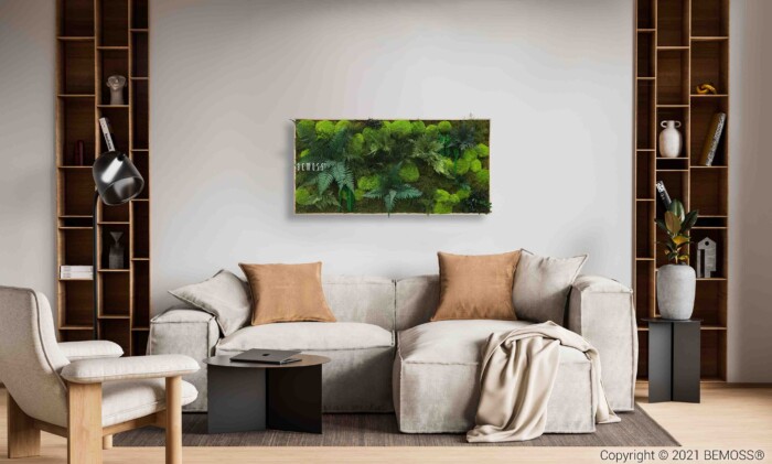 Un salon moderne avec un canapé sectionnel gris clair avec des oreillers beiges et gris et une couverture beige. Un Tableau de mousse PLANTES Acebo (Kópia) est accroché au-dessus du canapé. La pièce dispose d'étagères en bois des deux côtés avec des objets décoratifs et d'un lampadaire noir sur la gauche.